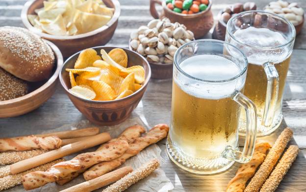 Tisch mit Biergläsern und verschiedenen Schälchen mit Chips, Nüssen und Brötchen